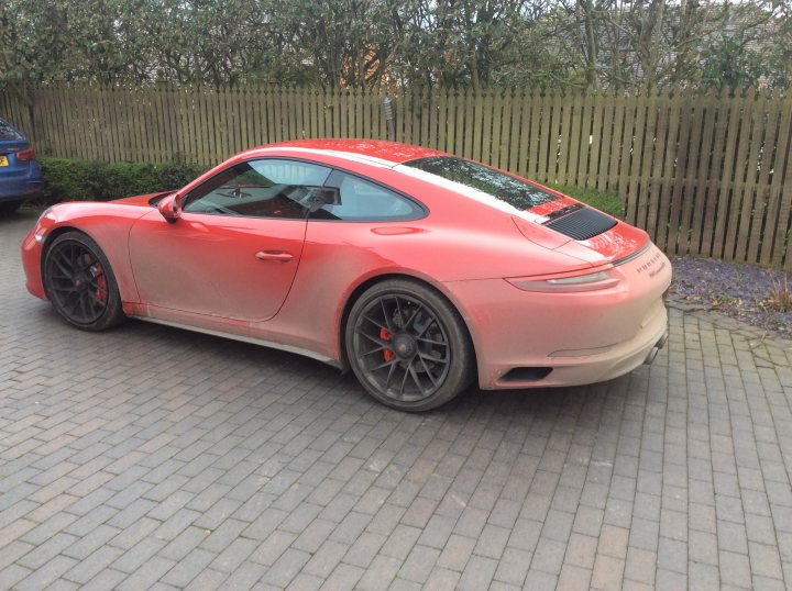 991 GTS Must haves - Page 177 - 911/Carrera GT - PistonHeads - The image shows a vintage looking car parked on a driveway. The car has a prominent spoiler at the back and is painted in a light orange or peach color with black rims. It features a convertible top that is folded down. The vehicle appears to be in good condition. In the background, there is a wooden fence and a portion of a blue car to the left, suggesting the driveway might be located in a suburban residential area.