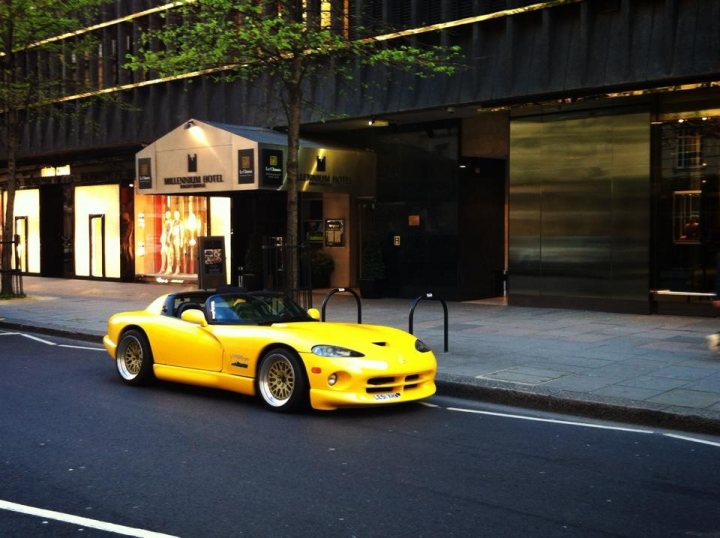 Ready for the summer - Page 1 - Vipers - PistonHeads - The image features a vibrant yellow Maserati sports car parked next to a sidewalk. The car is positioned diagonally, showcasing its sleek design and shiny exterior. Adjacent to the car is a sidewalk where shops and boutiques can be glimpsed, indicating that this scene might be in an urban area. Streetlights and buildings also add to the cityscape ambiance. The sky appears to be dark, suggesting it might be late afternoon or early evening. The overall setting seems to be a well-maintained city street during a time of cooler weather.