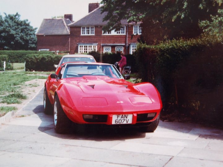The Official Corvette Picture thread. - Page 13 - Corvettes - PistonHeads - In the image, there's a vibrant red sports car parked on a street lined with hedges. The sports car is parked adjacent to a park and a residential area, with a person walking in the distance. The license plate of the sports car reads "FAN 607 YV". A white car is also parked in the background, and there's a house visible in the shot.
