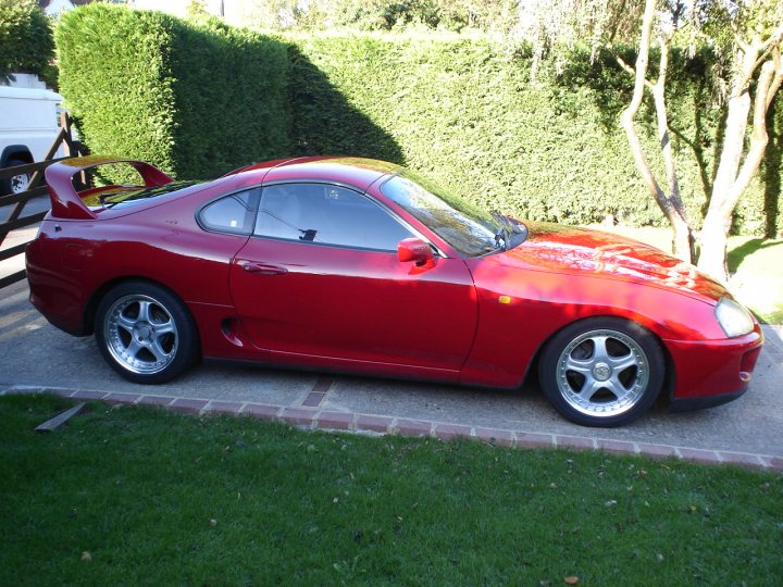 time we had pictures of everyones jap wagons - Page 137 - Jap Chat - PistonHeads - This image showcases a vibrant red sports car parked on a lush green lawn, indicating perhaps a private property or an exclusive club. The car strikes a dynamic pose with its rear side tilted to one side, implying motion or a very sharp turn. The side windows of the car are visible, reflecting the surroundings slightly. In the background, there are trees, a fence, and a building, suggesting this setting might be a residential area or a driveway of a housing complex. The clear day makes the colors pop, and the well-maintained lawn contributes to the overall elegance of the scene.