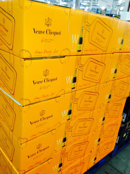 Bond's favourite Champage - Page 3 - Aston Martin - PistonHeads - This image features an assortment of champagne boxes prominently displayed for sale. The boxes are stacked high, showcasing the Veuve Clicquot brand and indicating that these are champagnes in various sizes. The champagnes appear to be a collection of different breeds from Veuve Clicquot, as suggested by the suggestions for dinner, implying that these are deluxe editions intended for special occasions or premium consumption. The layout of the boxes and wine bottles visible in some suggests a well-stocked retail environment, possibly a liquor store or a department in a grocery store with a focus on luxury goods.