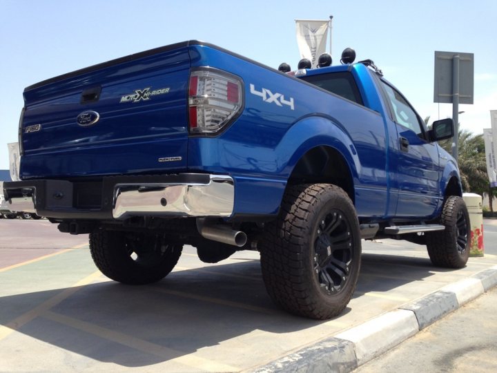 US Full Size Pickups - Page 1 - Middle East - PistonHeads - The image features a striking blue Ford F-150 XLT pickup truck, parked on a clear day. The truck is equipped with a four-door crew cab, sporting a chrome exhaust pipe that adds to its rugged appeal. Its black tires and well-defined fenders indicate a preference for off-road capabilities or perhaps simply a sense of style. The truck is parked in a lot, with typical orange and white traffic cones in the background, suggesting a road or parking area designed for public or commercial use.