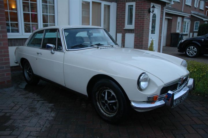 Pistonheads Hurt - The image shows a classic white Jaguar car parked on a brick driveway. In front of the car is a building, and the car is viewed from a slightly elevated angle. The setting appears to be in a residential area, as suggested by the presence of a neighboring house next to the driveway. The overall impression is of a quiet, suburban street scene.