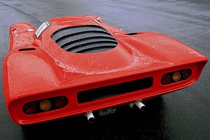 what's your favourite 'rear'? - Page 1 - Ferrari Classics - PistonHeads - This image shows a vibrant red vintage sports car parked on a road. The car's unique design features a distinctive front grille and round rear taillights, typical of classic sports cars. The wet surface of the road reflects the vehicle's sleek design, enhancing the overall appeal of the image. The focus is sharply on the car, while the background is blurred, drawing attention to the vehicle's details and elegance.