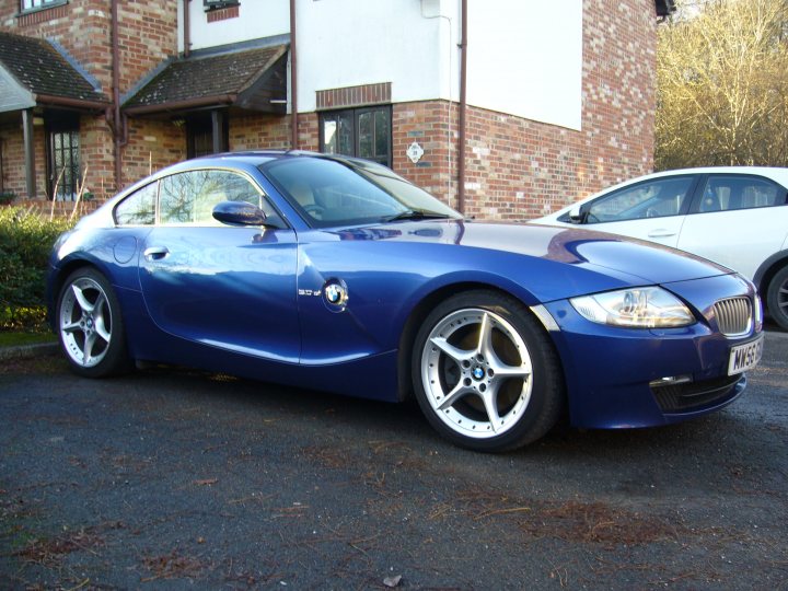 Z4 coupe si 3.0 pointers - Page 1 - BMW General - PistonHeads - The image features a striking blue BMW car parked on a residential street. The vehicle is positioned adjacent to a white car, enhancing a contrast of colors. The architecture of the house in the background exhibits a red brick facade, adding to the urban aesthetic of the scene. The driveway where the blue BMW is parked displays subtle signs of usage, with noticeable pine needles scattered about the ground, suggesting a recently driven upon surface.