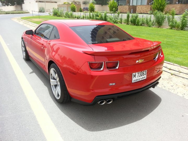 Pistonheads - The image displays a vibrant red Chevrolet Corvette C7 convertible car parked on the side of the road. The car is positioned at an angle to the camera, showcasing its sleek design and premium finishing. The license plate reveals that the vehicle is registered in Texas, as indicated by the distinctive format. The backdrop consists of a grassy area and houses, suggesting a residential suburban setting. The road on which the car is parked curves gently to the left, indicating a suburban street. Additionally, the yellow line on the road provides guidance for drivers regarding parking distance. This image captures the essence of a high-end sports car's presence in everyday life.