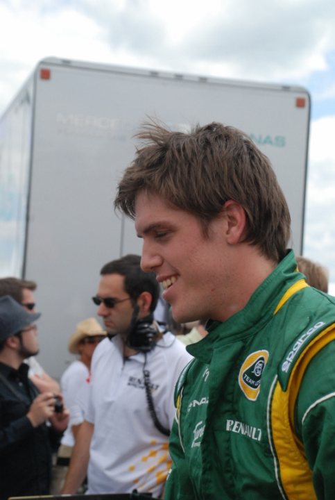 Pistonheads - The image features a man wearing a green racing suit with a prominent logo on the front, standing on a track. To his left, an individual appears to be conducting an interview, as suggested by the presence of a microphone. In the background, another person is also present, possibly a crew member or another participant in the event. The setting appears to be outdoors, indicated by the natural light and open space. The man in green seems to be engaging in conversation or being photographed, contributing to the dynamic atmosphere of the scene.