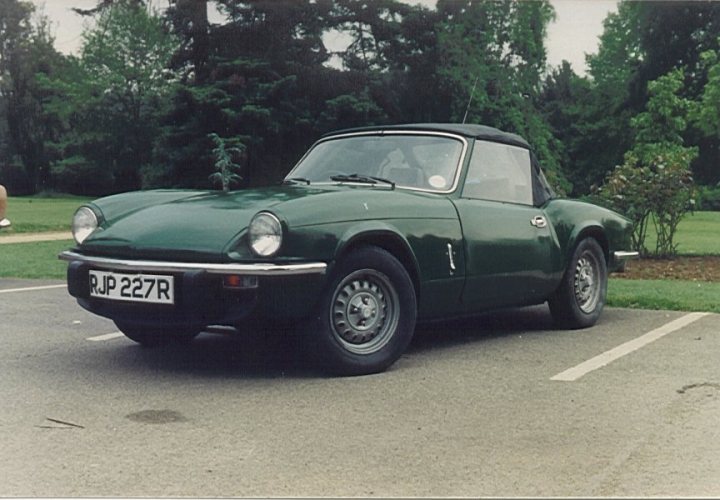 Spitfire/GT6 nose-in-the-air - Page 1 - Triumph - PistonHeads - The image shows a vintage British motorcar, likely from the 1960s or 1970s, parked in a gravel or dirt lot. The car has a vibrant green color with a black roof and a minimal amount of visible branding. It features round headlights, a distinctive flat-top front, and a split-style windshield. The vehicle is facing the camera, and the overall scene suggests it might be a sunny day, given the lighting on the car.