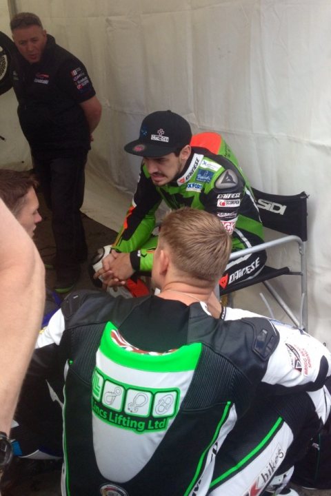 IoM TT 2014 - Page 48 - Biker Banter - PistonHeads - The image features two motorcyclists and another individual engaging in a discussion. The person in the center is wearing a motorcycle gear, and the other two individuals are standing close to him. They all appear to be engaged in a chat. The man in the center is a professional motorcyclist, as indicated by his attire and the design of his gear, which includes a company's logo. The setting is outdoors, possibly a motorcycle event or a pit stop, as suggested by the presence of tents and additional motorcyclists visible in the background.