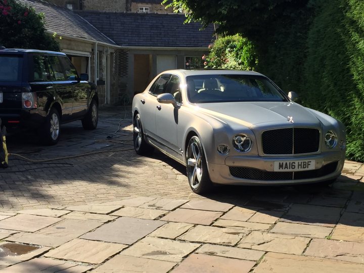 Range Rover L405 4.4 SDV8 or 3.0TDV6 - Quietest? - Page 1 - Land Rover - PistonHeads - This image shows a luxurious silver Bentley Flying Spur parked in a driveway of a residential property. The car is a four-door saloon and occupies most of the frame, signifying its prominence. In the background, there is a hedge, possibly part of the property's landscaping. There's another car, which appears to be a black SUV, parked to the left of the Bentley. The presence of the first car and the Bentley suggests that this is a privately owned driveway. The overall setting suggests a quiet, exclusive residential area.