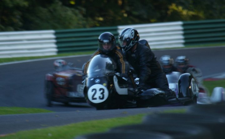 Vintage Motorcycle Club race pic's - Cadwell - pic heavy! - Page 1 - Biker Banter - PistonHeads - This image captures a dynamic scene of a motorcycle race. In the foreground, two motorcyclists are racing closely side by side, one slightly ahead of the other. Their vehicles are fastened with the number 23 prominently displayed. In the background, other motorcyclists are visible, partially obscured by the lead riders, indicating a hotly contested race. The venue appears to be a paved race track, as suggested by the grassy edge visible on the left side of the image. The atmosphere of the image conveys the intensity and high speed typical of motorcycle racing events.