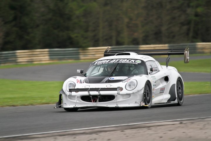 The big Elise/Exige picture thread - Page 6 - Elise/Exige/Europa/340R - PistonHeads - The image captures a thrilling moment on a race track. Dominating the frame is a white GT racing car, its sleek body gleaming under the track lights. The front end is adorned with a black aerodynamic blade, cutting through the air with precision. A large rear wing reaches upwards, hinting at the powerful drag that heralds. A black number "8" is proudly displayed on the side, adding to the competitive atmosphere. The backdrop is a blur of green and gray, suggesting the surrounding countryside, and the car is seen in motion on the tarmac, giving a slight drift as it zooms past. This is a snapshot of high-speed automotive racing, where every second counts.