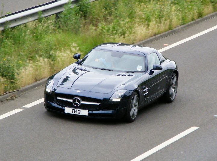 Herts, Beds, Bucks & Cambs Spotted - Page 332 - Herts, Beds, Bucks & Cambs - PistonHeads - The image shows a sleek, dark blue Mercedes sports car in motion on a road. The vehicle, which features a visible TH2 emblem and the brand's distinctive radiator grill, is adhering to speed limits indicated by lane markings painted on the road. The setting appears to be a high-speed route next to a grassy embankment. The side profile of the sports car is prominently displayed, clearly showcasing the vehicle's design as it travels at speed.