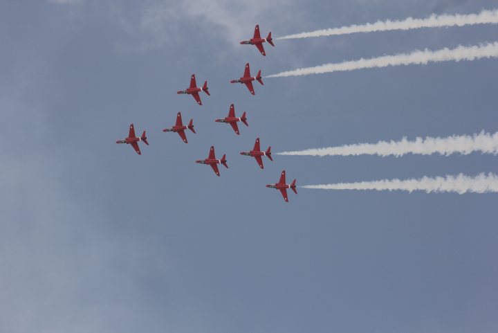 A group of planes flying in the sky - Pistonheads - The image captures a dynamic scene of nine jets painted in vibrant red, flying in tight formations against a backdrop of a cloudless, light blue sky. Each jet trails a stream of smoke typical of aerobatics performances, adding to the spectacle. Their formation suggests precision and teamwork, a common sight in airshows. The image conveys speed, discipline, and coordination, characteristic of such performances.