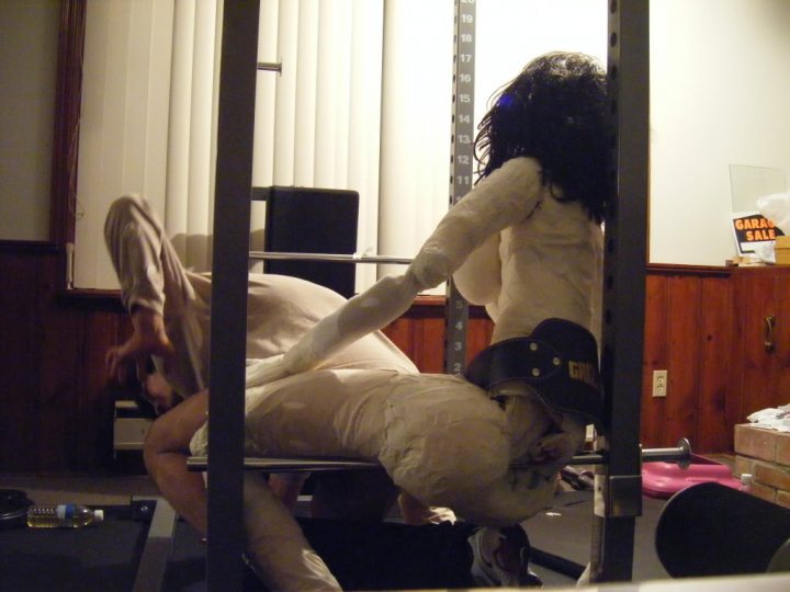 Give Nsfw Humannequin Pistonheads - This is a small and somewhat blurred image showing an indoor gym setting. In the foreground, two people appear to be involved in some kind of exercise activity. The person in the foreground is wearing what looks like a white protective clothing and is bent backwards; their hair is not visible due to the angle and blur. The second person, with black hair, is standing and facing the first person; their posture is upright, and their face or head is obscured as it's not in the frame. To the right and at the back of the scene, there is a wooden wall, over which a vertical workout board stretches. A weight bench and standard gym equipment are visible across the room. There are no visible texts or branding.