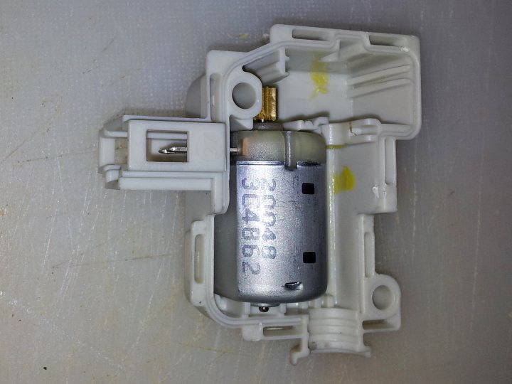 Boot locking solenoid kaput - Page 1 - Boxster/Cayman - PistonHeads - The image displays a close-up view of a small, white electronic device, which appears to be a part or component of a larger machine. The device has a metallic or silver plating on top and a barcode printed on its side, reading "2202,C1049," indicating a code for identification. The device contains several holes and a flap with a keyhole-like feature, which is closed. The image suggests the device may have a plug-like feature or connection, although it is not visible in the picture. The background is a white, possibly grained surface, which could be a workbench or a similar workspace.