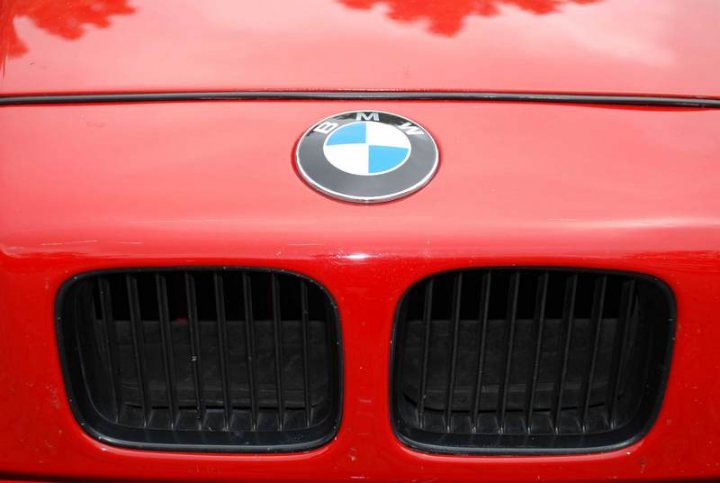 RE: PistonHeads Sunday Service: 25/07/10 - Page 9 - Events/Meetings/Travel - PistonHeads - The image shows the front of a red BMW car, viewed from a close angle that focuses on its distinctive grille. The grille consists of vertical black bars framing a blue and white BMW emblem. The car's sleek design suggests a sporty model, and the shiny surface reflects the environment, hinting at good condition.