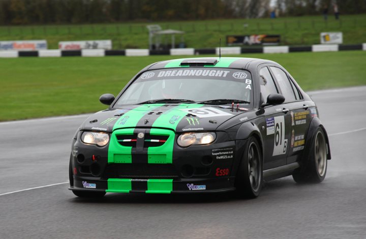 Pistonheads - This image captures an intense moment on a race track, featuring a modified black car adorned with green and black racing livery, bearing the word "Dreamedout." The car's exterior shines under the rays of sunlight, highlighting its sleek design and aerodynamic modifications. It's parked on a track, suggesting it's positioned for a high-speed drive, and the presence of a racer behind it indicates that the scene might be preparing for a thrilling race. The car's flashy design, coupled with the vibrant colors, adds to the overall excitement and anticipation of the event.