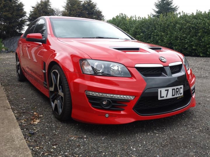 The Thunder from down under.... Holden HSV E2 GTS - Page 6 - HSV & Monaro - PistonHeads - The image showcases a red sedan parked on a gravel surface against a backdrop of trees. The car has a noticeable front spoiler and a sporty design, indicating it may be a higher-performance model. The license plate on the car reads "L7 DrC," which is likely to denote the individual car model rather than being a specific registration number. There is a slight reflection on the car's surface, suggesting a wet or shiny surface. The environment appears peaceful and natural, with the focus clearly on the car's design and condition.