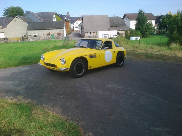 Early TVR Pictures - Page 35 - Classics - PistonHeads - In the image, a vibrant yellow vintage BMW sports car is parked on a driveway in a residential area. The car's sports outlook is further accentuated by the black and white pattern of the rims. The background reveals a serene suburban setting, with houses nestled amongst greenery. The car, being the only vehicle in the photo, exudes a sense of tranquility and elegance.