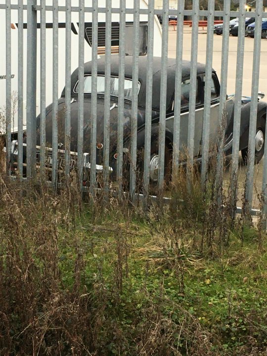 Classics left to die/rotting pics - Vol 2 - Page 414 - Classic Cars and Yesterday's Heroes - PistonHeads UK - The image shows a large, antique truck parked near a chain-link fence. The truck is predominantly black and features the word "Coca Cola" on its side. It's an old-style vehicle with a prominent front grille, suggesting it might be a vintage model from the early to mid 20th century. The background is out of focus, but it appears to be an industrial or commercial area as indicated by the fence and the structures behind it. There are no visible people in the image, and the style of the photo seems candid, possibly taken without intent to document the truck.