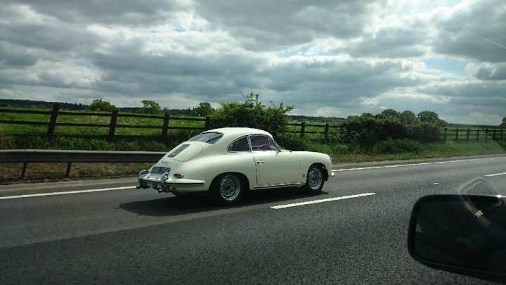 Supercars spotted, some rarities (vol 6) - Page 240 - General Gassing - PistonHeads - The image shows a small, white antique car traveling on a road with a clear sky filled with clouds in the background. The car is slightly blurred, indicating motion, and has a vibrant white color, typical of many classic airstreams. The road is bordered by a rural landscape, which includes a fence and a grassy area, enhancing the feeling of a countryside journey.