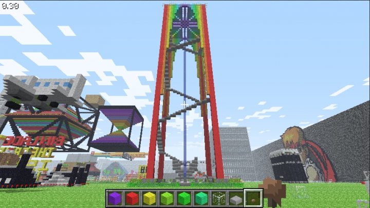 Rainbowfalljpg - This image appears to be a screenshot from the game "Minecraft." The central visual element is a brightly colored rollercoaster or tower with multiple levels. Above it, the sky is a light blue with lone clouds, suggesting an outdoor setting. Surrounding the tower and rollercoaster are various other buildings and structures constructed using the blocky aesthetic typical of the game, indicating a busy industrial or theme park area. The user interface elements in the bottom part of the image, including a health bar and block icons, indicate that the game is paused and possibly being built or crafted.