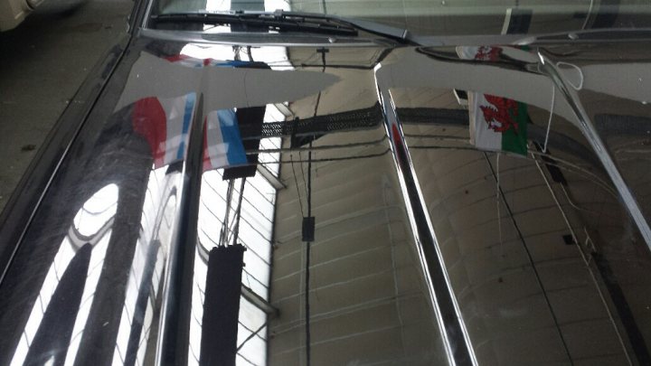 A view of a building from the window of a plane - Pistonheads - The image captures the polished hood of a car. The dark color of the car provides a reflective surface where several items are visible. There are at least two flags being reflected, featuring stripes and knot designs. A cell phone is also visible in the reflection, holding a peace of pizza. Additionally, a few wires or pipes are scattered across the hood. The reflection appears to be taken from inside the car, as the car's interior ceiling is visible at the top left corner of the frame.