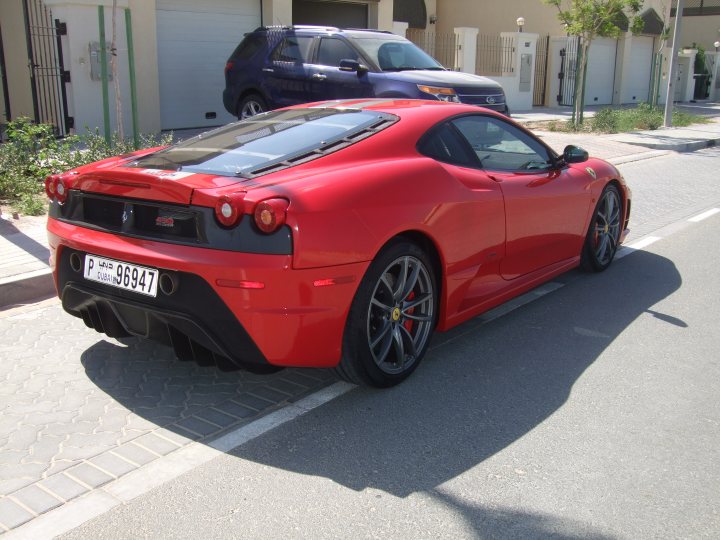 My First Ferrari...and its a Scud! - Page 1 - Ferrari V8 - PistonHeads - The image depicts a vibrant red Ferrari parked on a grey asphalt street. It's a convertible sports car, characterized by its black roof that contrasts with the car's bold color. The ground tilts due to the sharp angle of the photograph, giving a dynamic sense of movement. A white line is visible behind the car, marking the boundary of the parking space. The car is fully parked, occupying a significant portion of the frame.