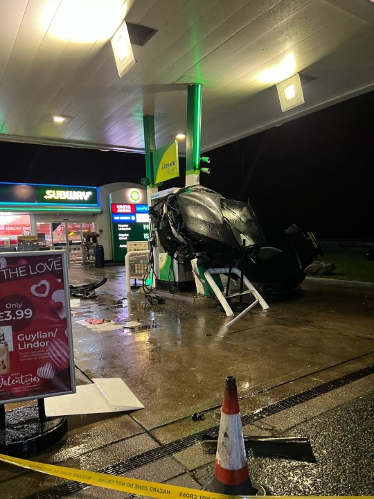 What Car Is This ? - Page 1 - General Gassing - PistonHeads UK - The image shows a dramatic scene at a gas station. A car is flipped upside down on the ground, indicating it has been involved in an accident. Surrounding the car is water and debris, suggesting that the car might have hit a nearby object or caused a spill. 

A sign advertising love coffee is visible, adding to the ordinary nature of the setting before the incident occurred. The gas station appears to be open with a lit sign outside. In the background, a convenience store is part of the gas station, and an emergency vehicle is present at the scene, hinting at the ongoing response to the incident. 

The photo captures the aftermath of a crash, showing the disruption caused by the accident on what would have been a routine day at the gas station.