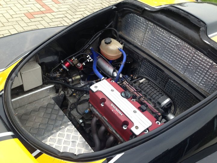 A close up of a luggage bag on a car - Pistonheads - The image presents an open hood of a high-performance sports car. A red engine block stands out, covered by a black grille with the car's logo imprinted on it. Numerous cables and hoses are visible, indicating the intricate mechanism within. The engine is likely fueled by the yellow tank, which is situated close to the engine. This top-down view reminds one of the complexity and precision required in motor vehicle engineering.