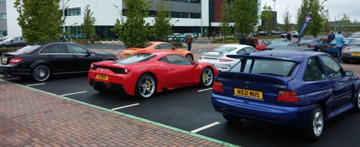 A car is parked on the side of the road - Pistonheads - The image shows a parking lot filled with parked cars. Amongst the various vehicles, there is one bright red car with the top down, which appears to be a sports car based on its design. Other cars are parked in neat rows, and there are individuals and trees in the background, suggesting a suburban or commercial setting. The overall scene indicates a clear day with ample parking space. Lastly, the presence of other cars and traffic lights implies that the image was taken on a busy day or in a busy area.