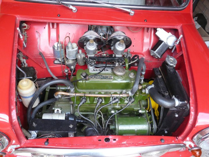 Suspension preparation for classic rallying - Page 1 - Classic Minis - PistonHeads - The image shows a red and black vehicle, possibly a compact car, with its hood open. The upper part of the engine bay is visible and appears to be somewhat dismantled or unfinished, with several mechanical components exposed. There's a prominent green engine block which contrasts with the surrounding parts. Above the engine, there's a visible alternator on the right side. The vehicle's interior litters the floor area, indicating that the vehicle might be in the process of being worked on or repaired.