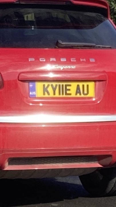 What C124PPY personalised plates have you seen? V01. 3 - Page 186 - General Gassing - PistonHeads UK - The image shows a red car parked outdoors. The vehicle is positioned at an angle, and its license plate is partially visible, displaying the letters "KYIE AU." The car appears to be a hatchback model with a distinctive design on the rear doors, which seems to feature a graphic of a face or mask. There's also a visible logo on the side, suggesting it might be a luxury vehicle, possibly a Porsche, as indicated by the "P" emblem in the background. The car is parked next to another vehicle that isn't fully visible within the frame of the image.