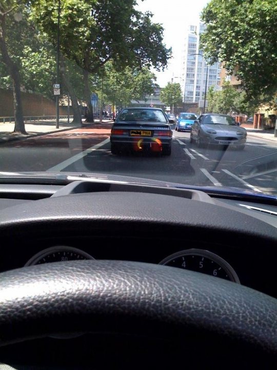 Spotted Rarities Pistonheads Supercars - The image showcases an urban street scene through the front windshield of a car. The dashboard of the car is visible alongside a steering wheel. On the street, several cars are traveling in different directions, giving the impression of a busy city street. Trees lining the street and distant buildings hint at a suburban area. The focus of the photograph is on the vehicles and the road ahead, providing a snapshot of everyday life in motion.