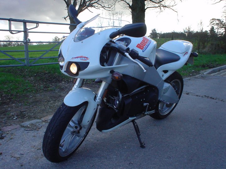 Owned Bike Pistonheads - The image showcases a white Suzuki motorcycle parked on a road in what appears to be a rural setting. The motorcycle is the focal point of the frame, with its prominent display of the brand name "Suzuki" on its body. The bike's sleek design and polished finish suggest it's in good condition. The surrounding greenery, including a field and a fence, give the scene a peaceful, country ambiance.