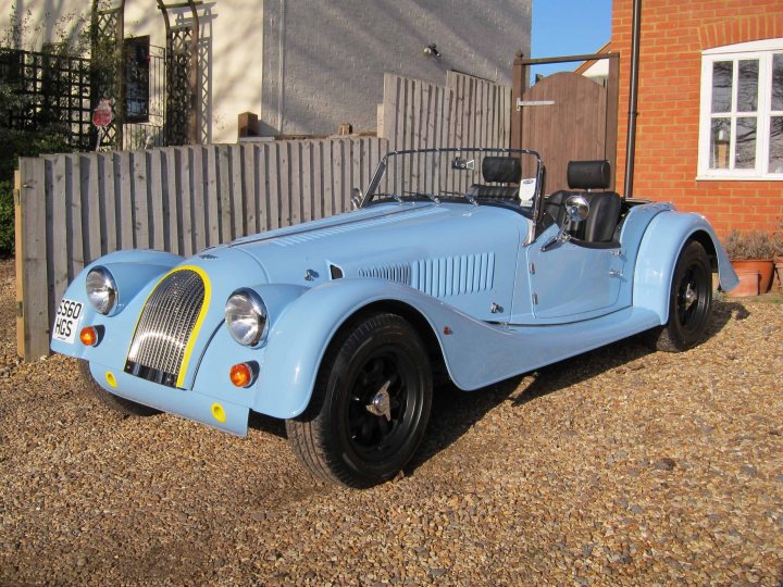 Pistonheads - The image features a vibrant blue sports car parked on a gravel driveway. The car has a classic design with round headlights, a prominent grille, and a convertible top. The wooden fence in the background adds a touch of rustic charm to the scene. A building can be glimpsed in the distant background, suggesting a residential setting. The image conveys a sense of serenity and elegance, with the blue car being the main focal point.