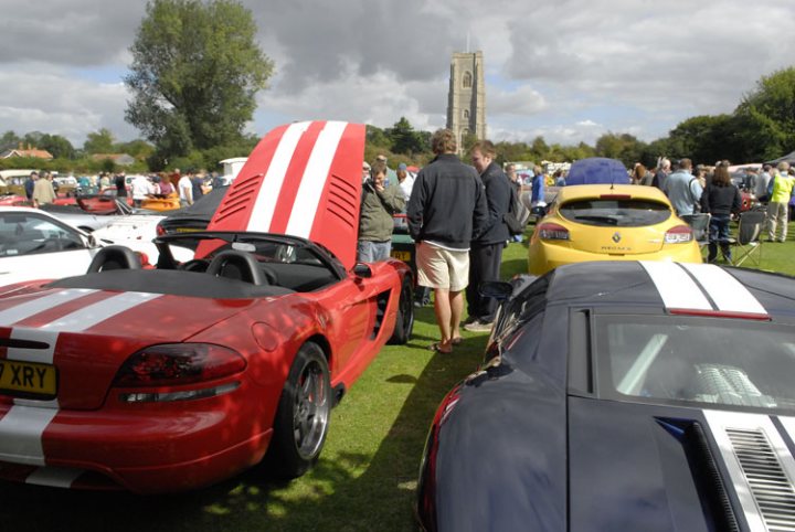 Anyone know this one - Page 1 - Vipers - PistonHeads - The image captures a lively scene at what appears to be a car show or event. Prominently featured in the frame is a red sports car with a black interior and a distinctive white stripe, giving it a sleek and unique look. 

Several people can be seen around the vehicles, walking around, examining the cars, and engaging in conversation. They are casually dressed, suggesting a relaxed and enjoyable atmosphere. 

The cars are parked on a lush green field, which contrasts beautifully with the colorful displays of classic and luxury models. 

In the background, a towering clock tower stands tall, providing a memorable and picturesque backdrop to the event.