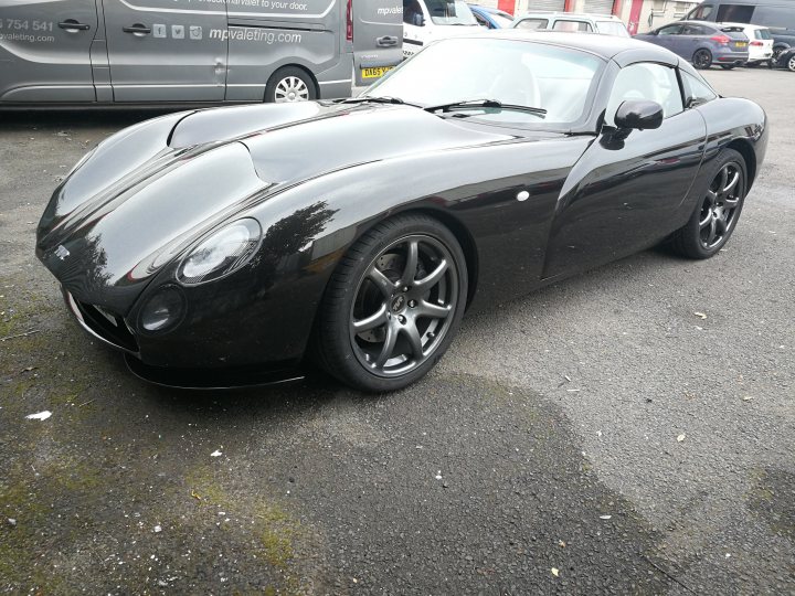 Spotted In South Wales (Vol 3) - Page 305 - South Wales - PistonHeads UK - The image features a black sports car parked in a lot. The vehicle is sleek and appears to be a convertible, given the absence of a roof. It has distinctive design elements such as a long hood, short rear deck, and large, circular headlights. The tires are fitted with five-spoke alloy wheels. The license plate reads "VR 02 ZF," which may indicate the model or registration details of the vehicle. In the background, there's another car and what seems to be a building or fence. The setting suggests an urban environment where cars are commonly parked. There's no text overlaying the image, and the focus is solely on the car itself.