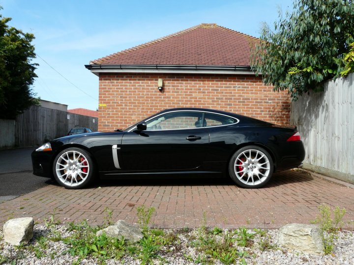 Pistonheads Xkr Weeks - The image showcases a striking black Porsche sports car parked in front of a brick building. The vehicle's sleek design and glossy finish are featured prominently. It's positioned in a driveway neatly paved with bricks. The building is constructed of red brick, and there's a small amount of greenery nearby, including a portion of a tree and some small plants. The sky visible in the background is clear, suggesting a sunny day.