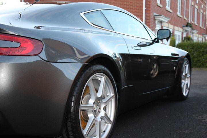 Driver Joins Fold Porsche Pistonheads Tvr - The image shows a sleek, modern black sports car parked on an asphalt driveway. The car's design includes a distinctive rear spoiler and five-spoke alloy wheels. Its shiny surface reflects the surroundings, suggesting a clean, polished condition. In the background, there's a brick building with white trim, adding to the urban feel of the scene. The car seems to be parked by the side of the road, located in front of the building.