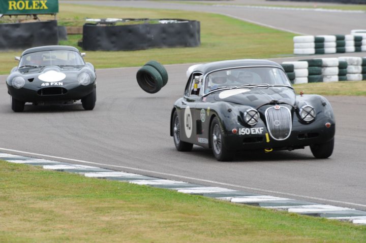 XKSS - Page 29 - Classic Cars and Yesterday's Heroes - PistonHeads - The image captures an exciting scene of a vintage race car competition. Two classic race cars, one predominantly black and the other white with blue accents, are in motion on a racetrack. The black car is ahead and appears to be overtaking the white car. Both cars have distinct racing numbers: 60 for the black car and 12 for the white one.

The race track itself is green and surrounded by grass, providing a natural backdrop to the high-speed competition. In the background, there are spectators observing the event, adding to the atmosphere of the competition. The presence of these elements suggests a professional vintage racing event, with participants and fans alike immersed in the thrilling action.