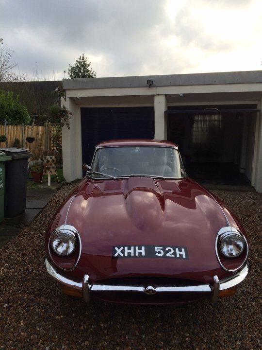 Get your Jags out - Show us your car - Page 12 - Jaguar - PistonHeads - The image shows an old red sports car parked in front of a garage or a large door with a decorative window design. The car is sleek and has distinctive headlights and a round, black license plate. The gravel in the foreground suggests a driveway or a paved area with gravel surface. The sky is cloudy, indicating overcast weather conditions. The style of the image and the vehicle suggest it might be an older or vintage model.