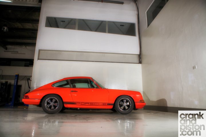 The 912 is done.. kinda - Page 1 - Middle East - PistonHeads - In the image, a vibrant orange Porsche 911 Turbo sits parked against a clean, white wall. The car is positioned in front of a building that features a window lattice, adding an interesting texture to the background. The Porsche is equipped with wheels and tires, ready to hit the road. The overhead angle of the photo provides a clear view of the car's design and color. The absence of other objects or vehicles in the image puts the focus entirely on the Porsche.