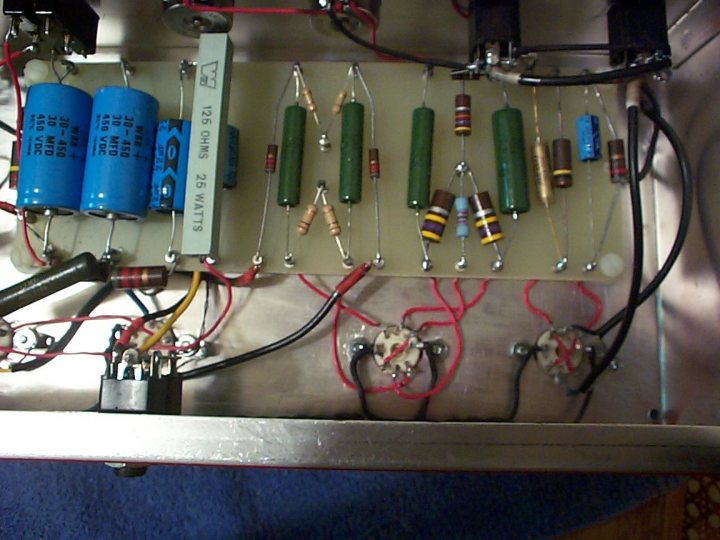 The image depicts an intricate assembly of electronic components. Dominating the scene are multiple cylindrical capacitors of different sizes, neatly arranged in a row. They are connected to a metal plate or board, which is the focal point for the other components. Surrounding the capacitors, wiring can be seen, creating a complex network that seems to spin a story of an internal combustion engine's electrical system. Two potentiometers, positioned near the top of the image, rest parallel to each other, suggesting control or adjustment of the system's parameters. The entire setup is presented in a close-up, allowing for a detailed inspection of the components and their interconnections.