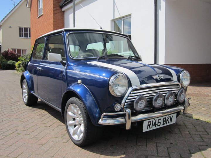 An old car is parked in front of a house - Pistonheads - The image shows a classic convertible mini car parked on a paved driveway. The vehicle has a blue exterior with a white roof and is marked by a silver stripe down its side. It is trimmed with chrome and features round headlights and round tail lights. There is a license plate at the front, and the car presents a vintage style. The background reveals a building, suggesting that the car is parked in a residential area.