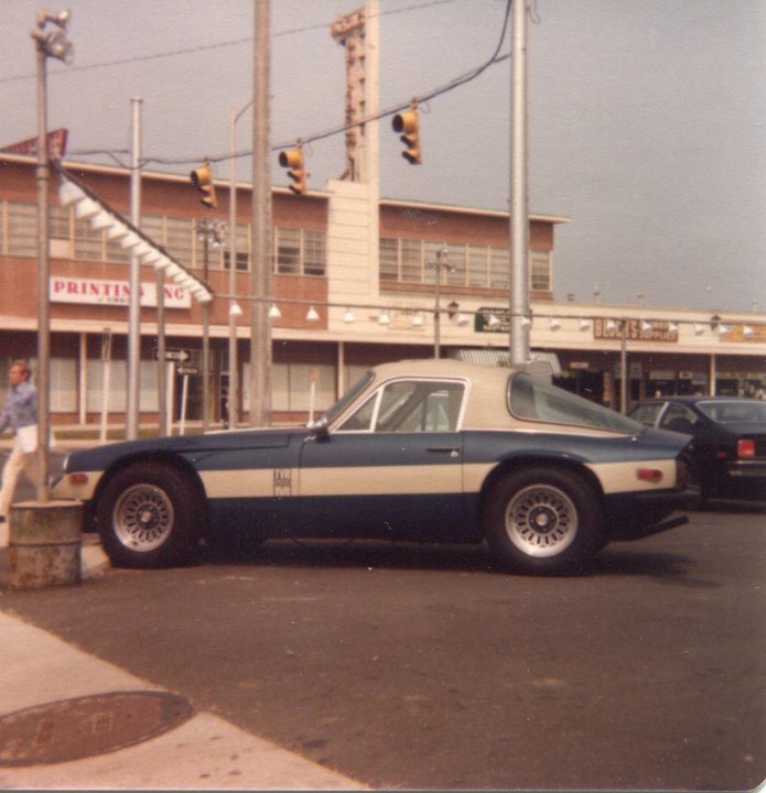 Early TVR Pictures - Page 4 - Classics - PistonHeads - The image depicts an urban scene with a parking lot. The main focus is a vintage sports car, characterized by its striped design and two doors. The car is parked on the asphalt, facing towards the right side of the frame. Behind the car, there is a building and traffic lights on poles, suggesting a well-regulated traffic system. The quality of the image appears to be slightly vintage, with a faded and grainy appearance. The atmosphere suggests it might be a nice day, possibly in late afternoon, given the soft lighting.