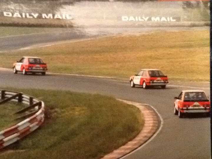 A truck driving down a road next to a forest - Pistonheads - The image depicts a dynamic racing scene at what appears to be a motor race track. There are multiple cars in the frame, with three prominently featured in the center, racing each other at high speeds. The cars are colored in shades of white, yellow, and red, with one car having orange detailing. The track itself is lined with red and white safety barriers and is bordered with grass, suggesting a well-maintained venue for the sport. Above the race track, the sky is relatively clear, and the entire scene is captured from an aerial perspective, giving a broad view of the ongoing event. The atmosphere is charged with adrenaline and competition as the cars navigate the track at high speeds.