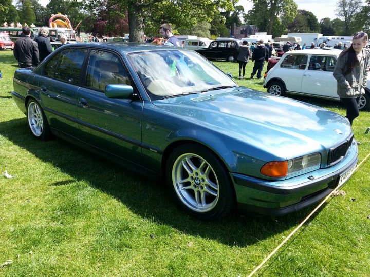 Thirlestane Castle Classic Car Show - Page 1 - Scotland - PistonHeads - In this image, a green BMW car is parked on a grassy field. It's a 2-door model with a sunroof, and the photo gives it a vibrant, almost sparkling appearance due to the sunlight reflecting off its glossy exterior. The BMW is the main subject of the photo, and its sleek design stands out against the green backdrop. In the background, several other cars and people are visible, suggesting that this might be an outdoor car event or a social gathering in a park.