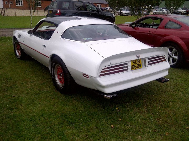 Pistonheads - The image showcases a vintage white sports car parked in a grassy field. The car's body is untouched, preserving the original design of white, black, and red stripes. Its license plate reads "SUB 96W." In the background, a red car is also parked, adding to the scenic and picturesque setting.